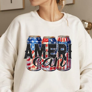 May include: White sweatshirt featuring a graphic of three beverage cans with a patriotic American flag design. The word "AMERICAN" is printed in bold, distressed black letters across the cans, with a cursive "can" underneath.