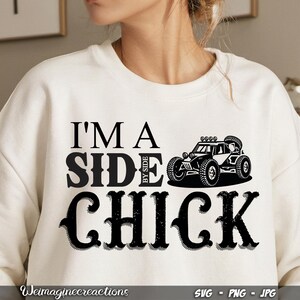 May include: White sweatshirt with black text that reads "I'm a Side by Side Chick" and a black silhouette of a side-by-side vehicle.