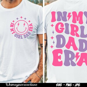 May include: White t-shirt featuring a pink and purple graphic that reads "In My Girl Dad Era" with a lightning bolt. The graphic is in a retro style font.