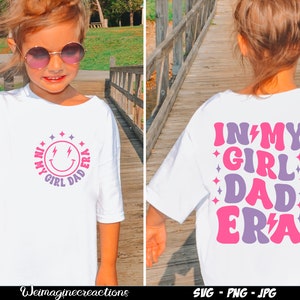 May include: A white t-shirt with a pink and purple design that says "In My Girl Dad Era" on the back and a smiley face with lightning bolts and the same text in a circle on the front.