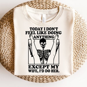 May include: A white t-shirt with a black graphic of a skeleton doing a yoga pose. The text on the shirt reads "Today I don't feel like doing anything except my wife, I'd do her."