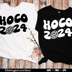 Puede incluir: Dos camisetas, una blanca y otra negra, con el texto "HOCO 2024" en una fuente retro y un diseño de bola de discoteca. Las camisetas se muestran sobre una superficie de madera.