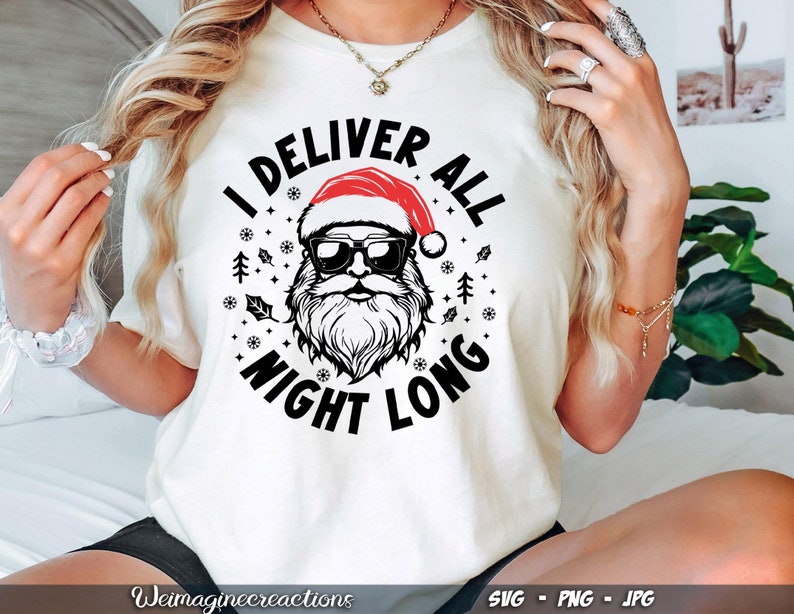 Puede incluir: Camiseta blanca con un gr&aacute;fico negro y rojo de Pap&aacute; Noel con el texto "I Deliver All Night Long".