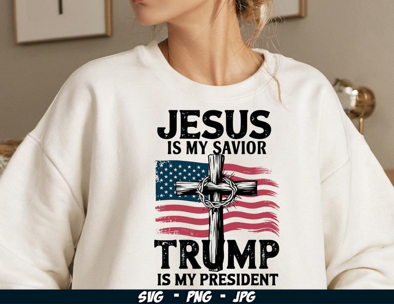 May include: White sweatshirt with a graphic design featuring a cross with a crown of thorns, an American flag, and the text "Jesus is my Saviour Trump is my President".