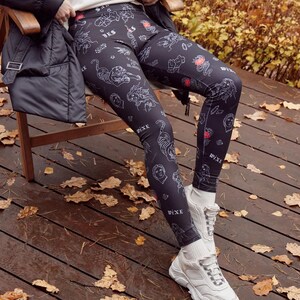 May include: Black leggings with a white tattoo-style print featuring tigers, roses, and other designs. The leggings have the word "WIXE" printed on the side. The person is wearing white trainers.
