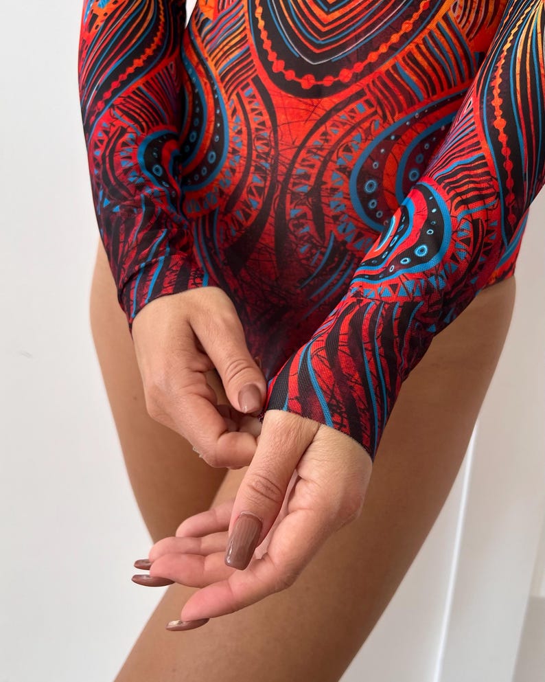 May include: A long-sleeved bodysuit with a vibrant, intricate pattern in red, black, and blue. The design features swirling shapes and geometric elements. The fabric appears to be a lightweight, stretchy material.