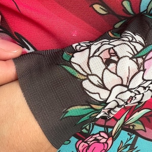 Peut inclure: Gros plan sur un tissu rouge et noir avec un motif floral. Le tissu est transparent et a une texture de maille. Les fleurs sont blanches, roses et vertes.