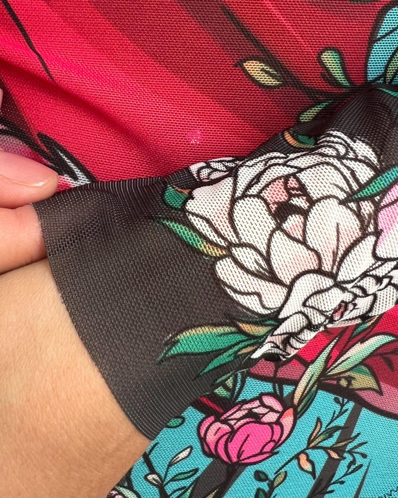 Peut inclure: Gros plan sur un tissu rouge et noir avec un motif floral. Le tissu est transparent et a une texture de maille. Les fleurs sont blanches, roses et vertes.