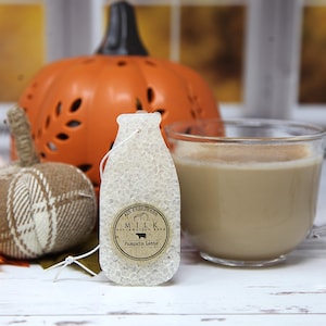 May include: A milk bottle-shaped air freshener with a textured, translucent white surface and a white hanging string. A circular tan label features the text AIR FRESHENER, MILK RECLAMATION BARN, and Pumpkin Latte with a small cow silhouette icon.