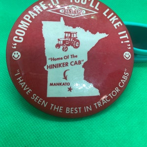 Puede incluir: Botón rojo y blanco con un mapa de Minnesota, un tractor y el texto "COMPARE IT - YOU'LL LIKE IT!" "Home Of The HINIKER CAB" MANKATO "I HAVE SEEN THE BEST IN TRACTOR CABS"
