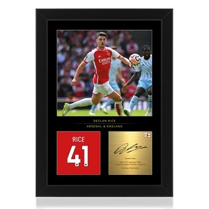 May include: A framed photo of Declan Rice, a soccer player, wearing a red and white Arsenal jersey. The photo is surrounded by a black frame and includes a red jersey with the number 41 and a gold plaque with Rice's signature and information.