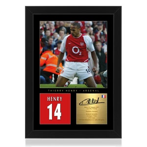 Op de afbeelding: Een ingelijste foto van Thierry Henry, een professionele voetballer, die een rood-wit Arsenal-shirt draagt met nummer 14 op de rug. De foto is geplaatst tegen een zwarte achtergrond met een gouden inscriptie die "Thierry Henry - Arsenal" luidt. De inscriptie bevat ook Henry's handtekening, zijn geboortedatum en een lijst van zijn Arsenal-onderscheidingen.