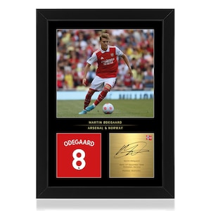 May include: Framed photo of soccer player Martin Ødegaard in his Arsenal uniform, with his jersey number 8 and signature on a gold background.