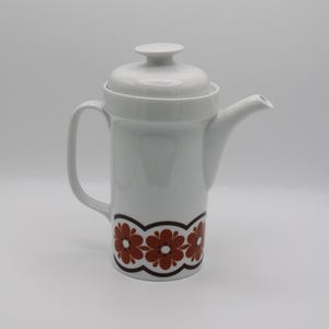 May include: White ceramic coffee pot with a brown floral design around the base. The pot has a lid and a handle.