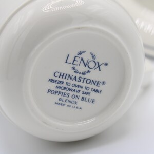 May include: The bottom of a white ceramic mug with blue lettering that reads "LENOX&reg; CHINASTONE&reg; FREEZER TO OVEN TO TABLE MICROWAVE SAFE POPPIES ON BLUE LENOX MADE IN USA"