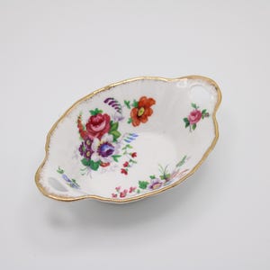 May include: A white porcelain bowl with a floral design and gold trim. The bowl has two handles and is oval shaped.