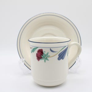 May include: A white ceramic teacup and saucer with a floral design. The cup has a blue rim and a blue and green floral pattern with red flowers. The saucer has a blue rim and a white center.