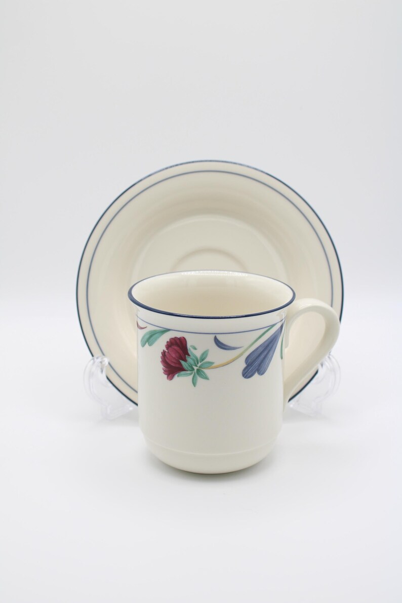 May include: A white ceramic coffee cup with a blue rim and floral design. The cup is sitting on a matching saucer with a blue rim.