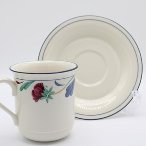 May include: A white ceramic coffee cup and saucer with a floral design. The cup has a blue rim and a blue and green floral pattern. The saucer has a blue rim and a white center.