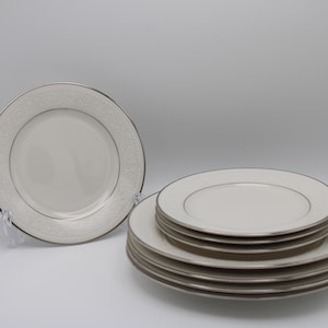 May include: A set of white ceramic dinner plates with a silver rim and a delicate floral pattern. The plates are stacked on top of each other.