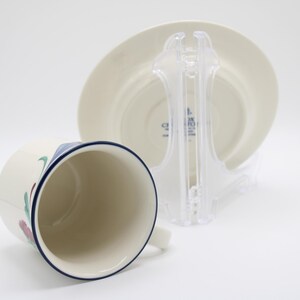 May include: A white ceramic teacup and saucer with a blue rim and floral design. The saucer has the text "CORKSCREW" printed on the bottom.