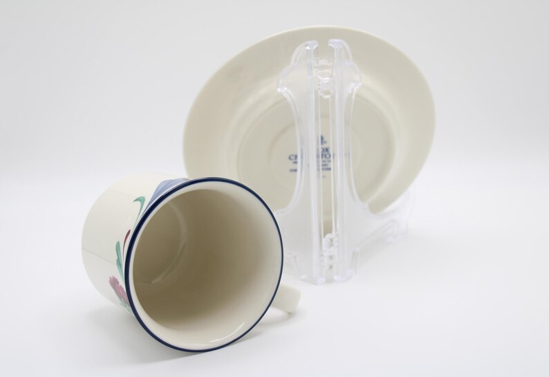 May include: A white ceramic teacup and saucer with a blue rim and floral design. The saucer has the text "CORKSCREW" printed on the bottom.