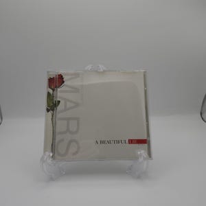 May include: A music CD case featuring the album A Beautiful Lie by Thirty Seconds to Mars. The cover art displays a single red rose on a stem against a light background, with the text MARS printed vertically and A BEAUTIFUL LIE horizontally.