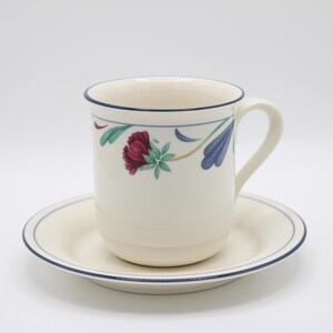 May include: A white ceramic coffee cup with a blue rim and floral design. The cup is sitting on a matching saucer.