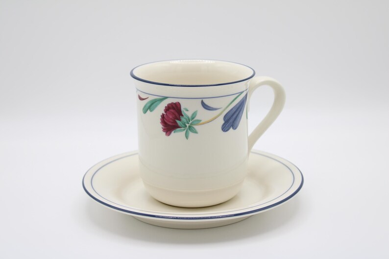 May include: A white ceramic coffee cup with a blue rim and floral design. The cup is sitting on a matching saucer.