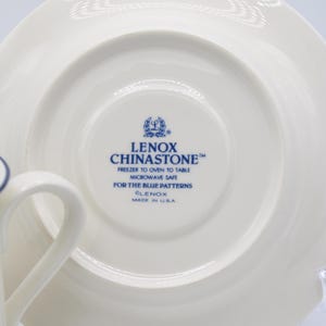 May include: A white saucer with a blue rim and a blue Lenox Chinastone logo. The logo reads "Lenox Chinastone", "Freezer to Oven to Table", "Microwave Safe", "For the Blue Patterns", "Lenox", and "Made in USA".