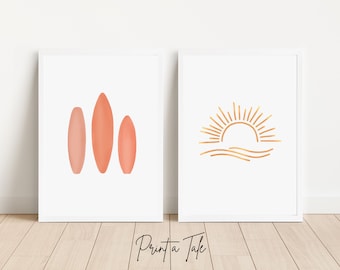 Puede incluir: Dos impresiones enmarcadas con un diseño minimalista. La primera impresión presenta tres tablas de surf de color coral. La segunda impresión presenta un contorno dorado de un sol poniéndose sobre el océano.