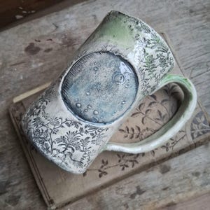May include: A set of three ceramic mugs with a speckled, matte finish. The mugs are in shades of cream, light gray, and dark gray. Each mug has a simple, minimalist design, perfect for coffee or tea.