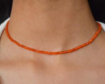 May include: A delicate orange beaded choker necklace. The necklace is made of small, round beads that are strung together on a thin cord. The necklace is simple and elegant, and it would make a great addition to any jewelry collection.