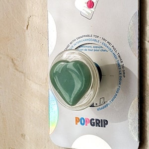 May include: A green heart-shaped PopSocket phone grip with the text "POPGRIP" on the packaging.