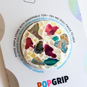 May include: A PopSockets PopGrip with a mosaic design featuring colorful pieces in red, green, blue, and yellow. The PopGrip is attached to a white backing with the PopSockets logo and product information.