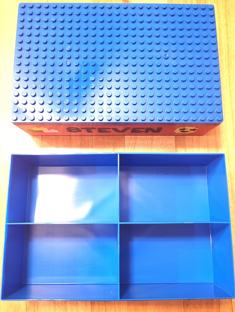 May include: Blue plastic storage box with a blue Lego base plate lid. The lid has the name "STEVEN" printed on it. The box has four compartments inside.