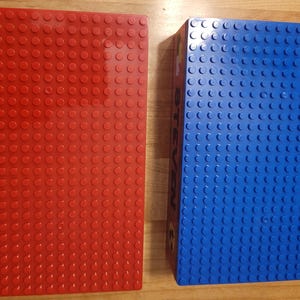 May include: Two square Lego baseplates, one red and one blue. The baseplates are made of plastic and have a textured surface.