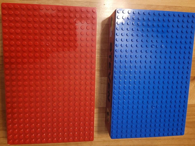 May include: Two square Lego baseplates, one red and one blue. The baseplates are made of plastic and have a textured surface.