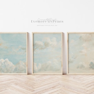 Puede incluir: Conjunto de tres impresiones de arte de pared vintage imprimibles que presentan una pintura de acuarela de un cielo azul con nubes blancas.