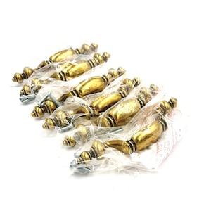 May include: A set of eight brass-colored cabinet pulls, each individually wrapped in clear plastic. The pulls have a decorative, ornate design with a central barrel shape and rounded ends. Each pull includes mounting screws.