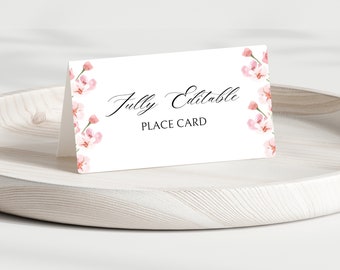 May include: A white place card with the words "Fully Editable PLACE CARD" in black script. The card is decorated with watercolor pink floral accents. The card is displayed on a light wooden tray.