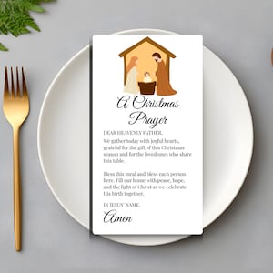 Könnte beinhalten: Eine rechteckige weiße Karte mit einer Krippendarstellung oben und dem Text A Christmas Prayer, Dear Heavenly Father, We gather today with joyful hearts, grateful for the gift of this Christmas season, und Amen.