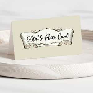 May include: A folded place card with the text "Editable Place Card" in a decorative banner design. The card is light beige and rests on a wooden tray. The banner is beige with black text.