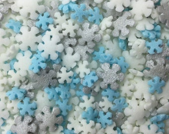 May include: A close-up of a variety of snowflake sprinkles in white, light blue, and silver. The sprinkles are perfect for decorating cakes, cupcakes, and other desserts.