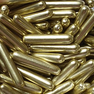 May include: A close-up image of a pile of gold-coloured sprinkles. The sprinkles are long and thin, with a slightly rounded end. They are perfect for decorating cakes, cupcakes, and other desserts.