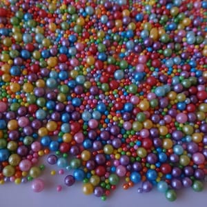 May include: A mix of colourful pearl sprinkles and smaller round sprinkles. The sprinkles are a variety of colours, including red, orange, yellow, green, blue, purple, and pink.
