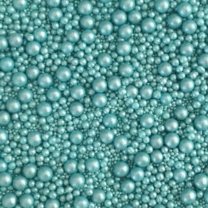 May include: A close-up image of a variety of teal blue pearl sprinkles. The sprinkles are of different sizes and are perfect for decorating cakes, cupcakes, and other desserts.