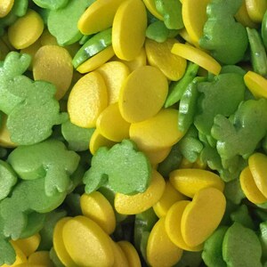 May include: A close-up of yellow and green sprinkles. The sprinkles are shaped like small circles and leaves.