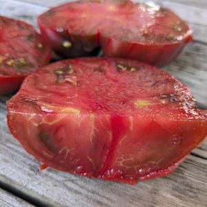 May include: Close-up of sliced heirloom tomatoes, showcasing deep red flesh with visible seeds and intricate internal patterns. The tomatoes are cut, revealing their juicy texture. The image highlights the natural colors and textures of the fresh produce.