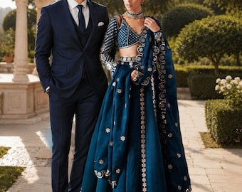 Può includere: Un completo a tre pezzi blu scuro con camicia bianca e cravatta, e un set lehenga color verde ottanio profondo con blusa a maniche lunghe, gonna lunga e dupatta abbinata, decorato con intricati ricami e dettagli a specchio argentati.